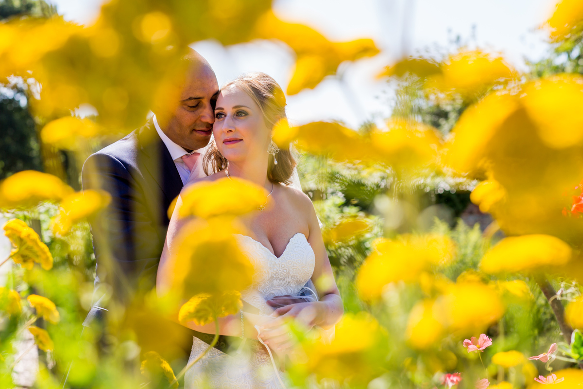 interesting perspective of newlyweds behind flower - shot by Kelmarsh Hall wedding photographer