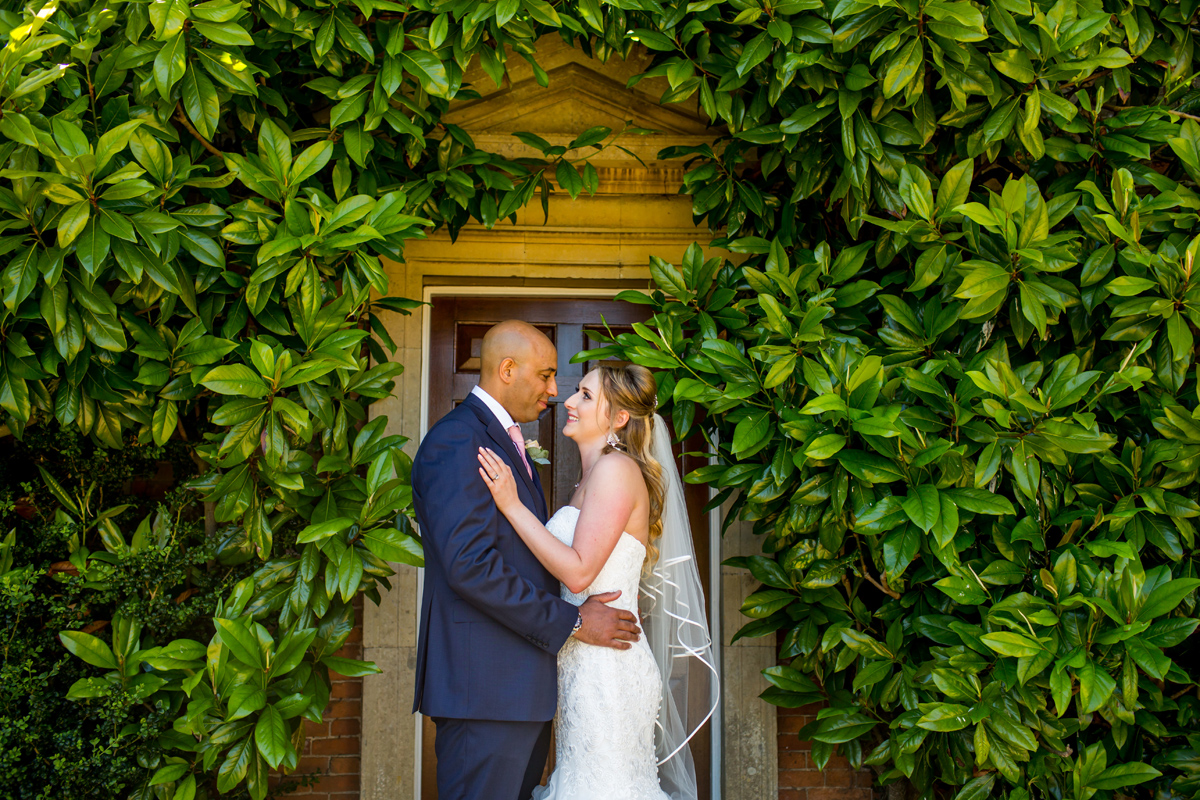bride and groom hold each other against a contrasting garden background, captured by Kelmarsh Hall Wedding Photographer