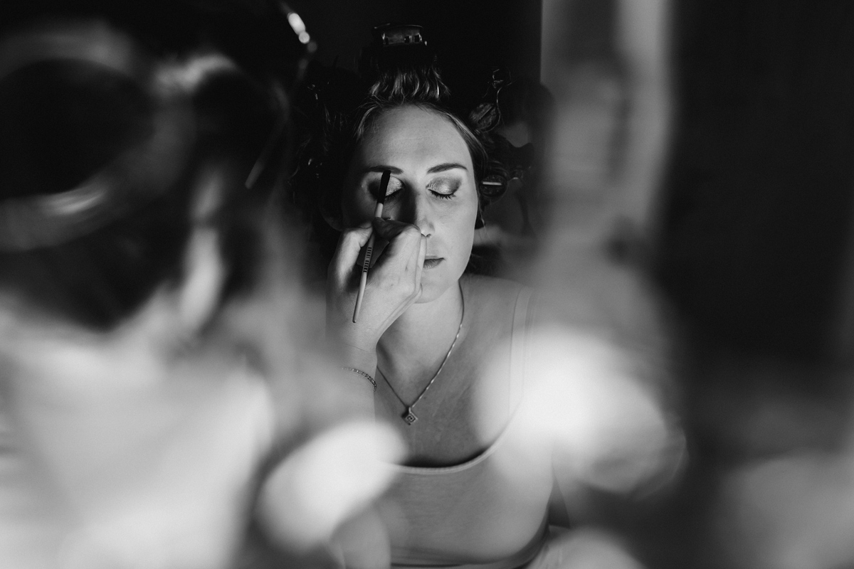 bride has her makeup applied in a black white shot captured by Kelmarsh Hall wedding photographer