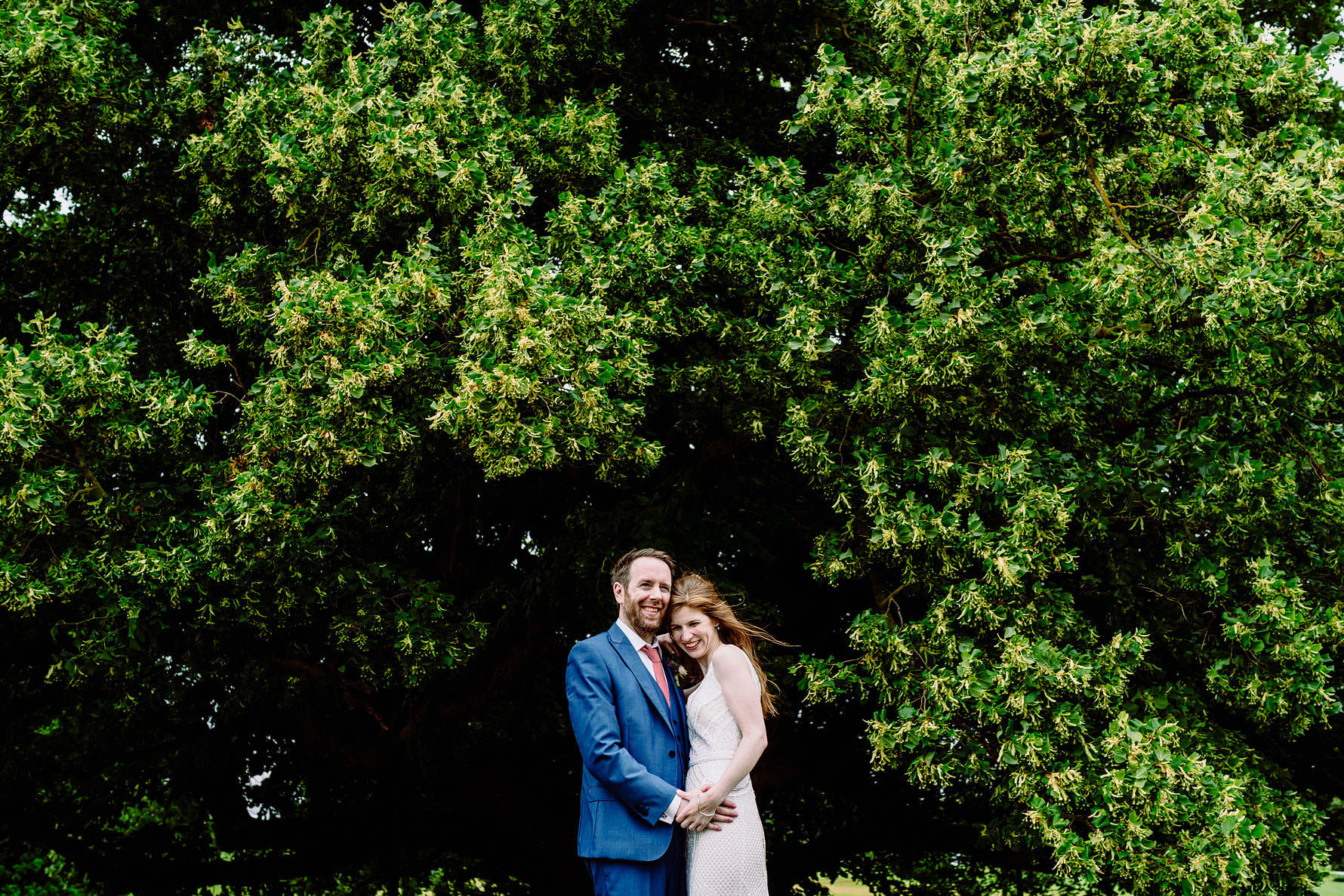 a bride and groom stood next to a tree